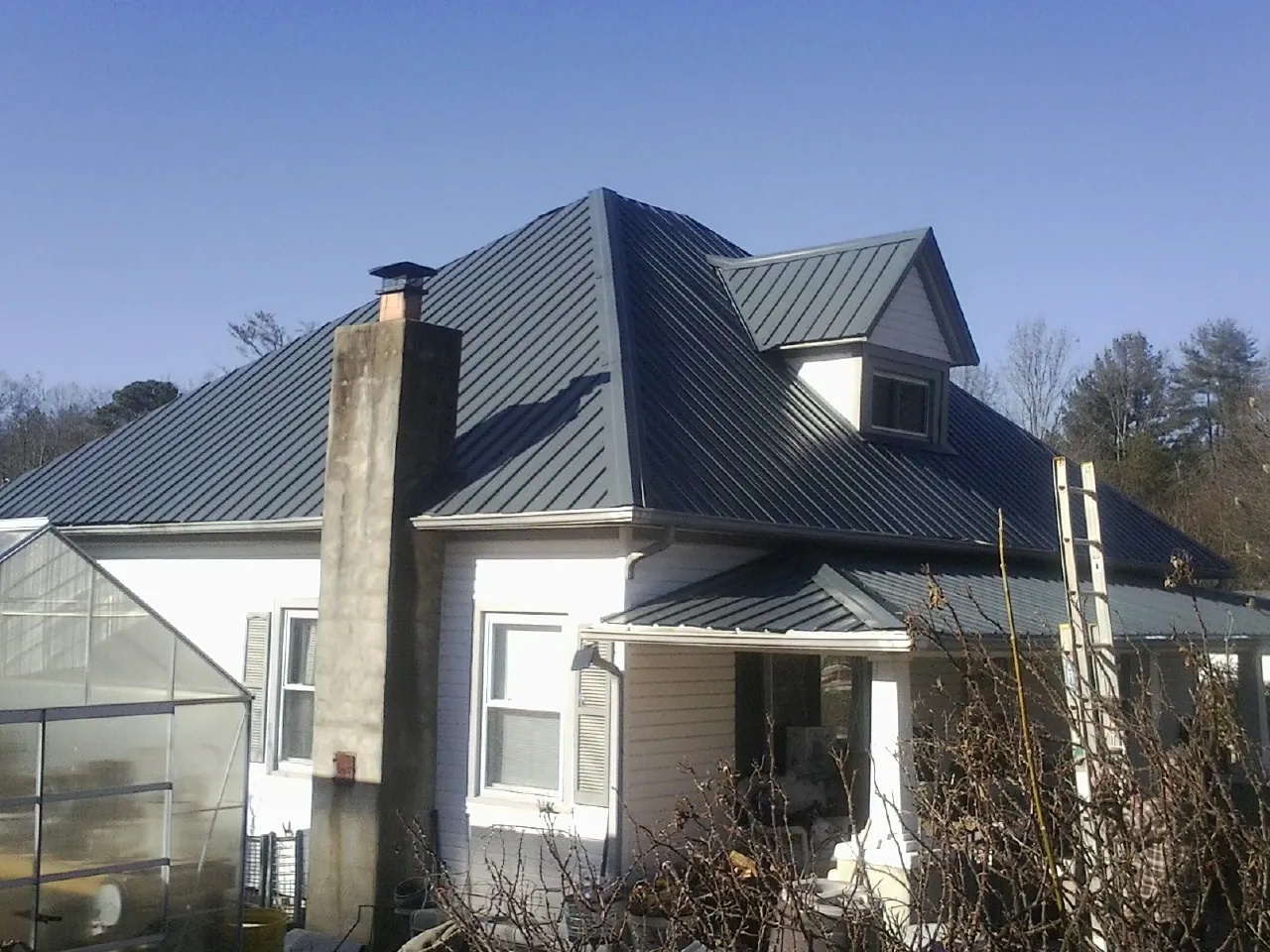 Dark blue standing seam metal roof on a white farmhouse with dormer — Slate & Tile Roof Repair by Roofing Brothers in Rochester