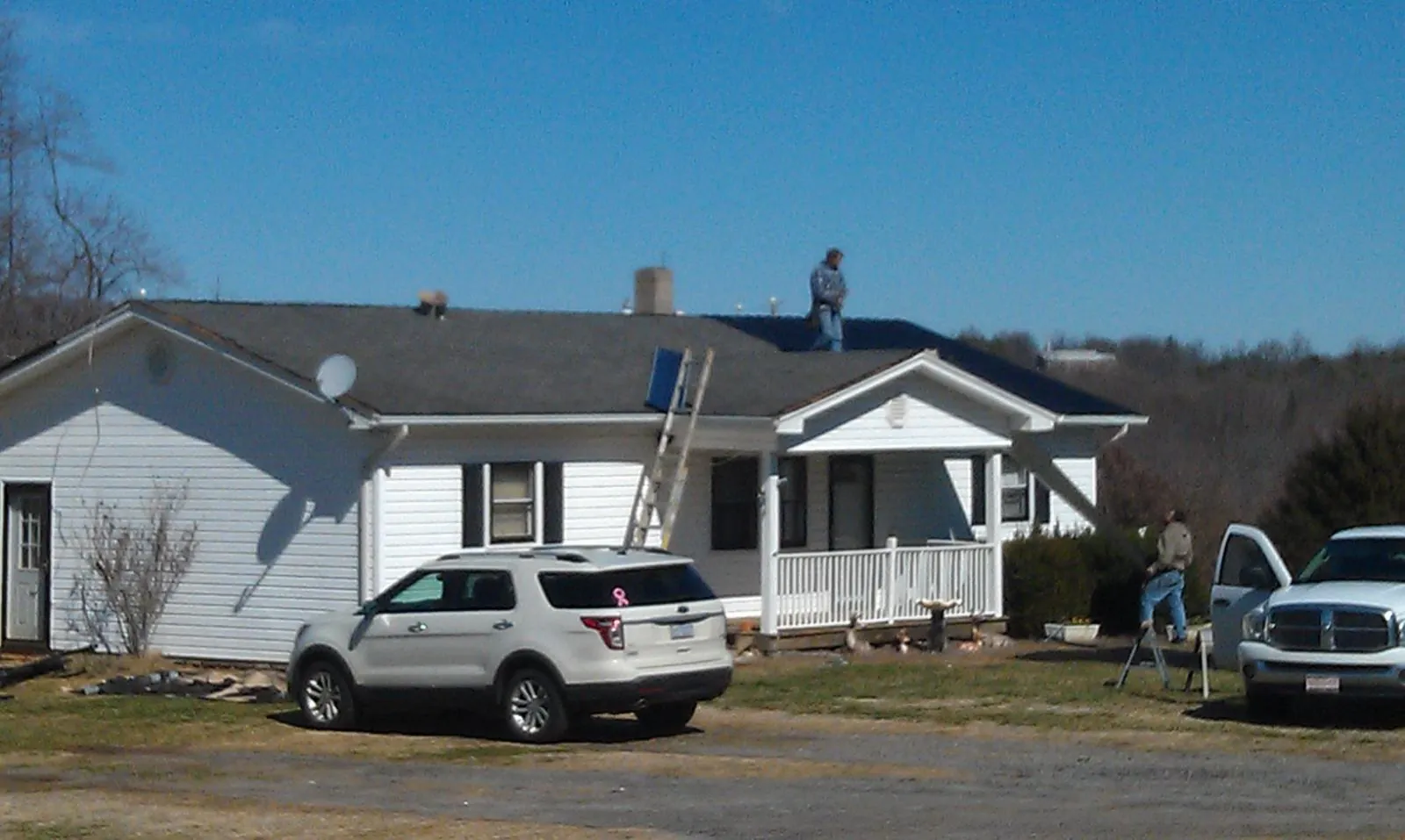 Roofers stripping shingles from a white ranch house roof in Rochester